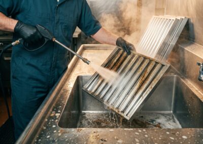 Technician pressure-washing greasy stainless steel kitchen hood baffle filters
